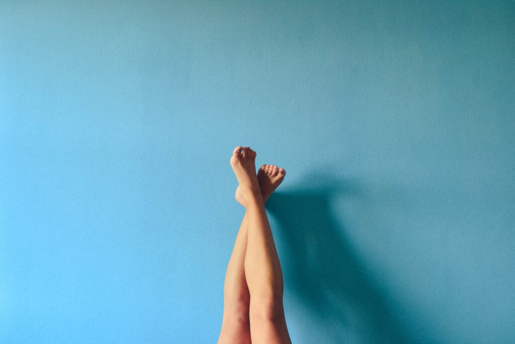 Weibliche Beine, im Liegen hochgestreckt und an eine blaue Wand gelehnt